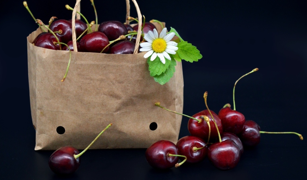 Бумажный пакет с ягодами черешни на черном фоне