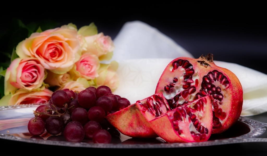 Гранат с виноградом на столе с букетом роз 