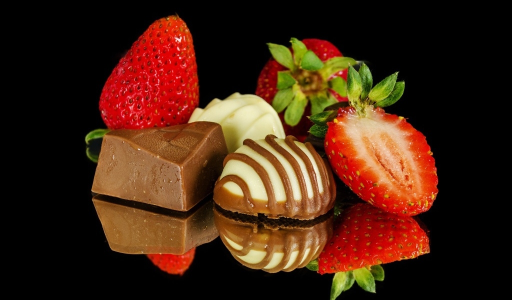 Красная клубника с шоколадными конфетами на черном фоне