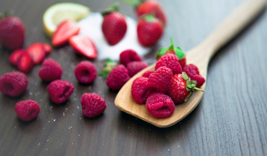 Спелая красная малина с деревянной ложкой на столе