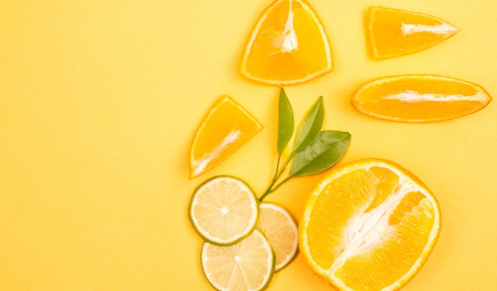 Нарезанные плоды апельсина и лайма на желтом фоне