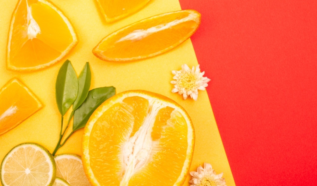 Кусочки апельсина и лайма на разноцветной поверхности 