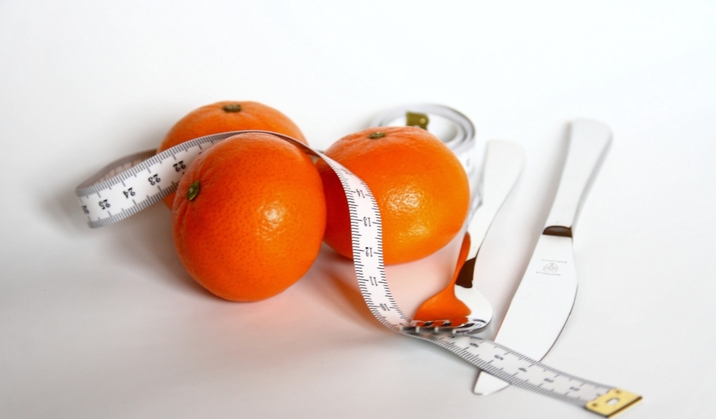 Мандарины с сантиметром и столовыми приборами на белом фоне