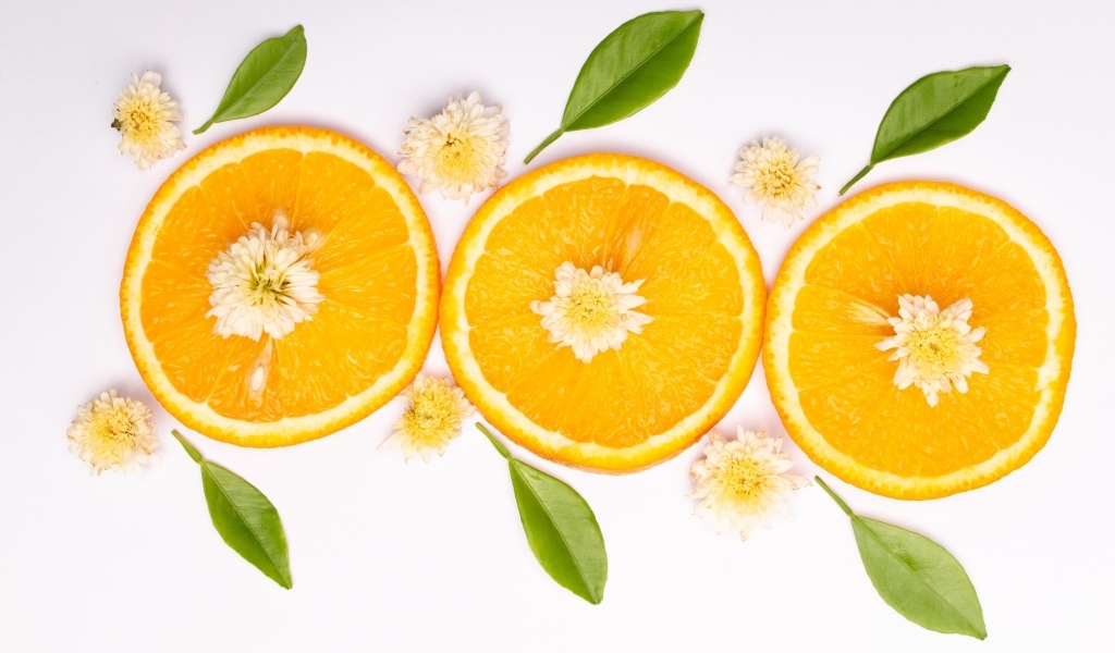 Три кружочка апельсина на белом фоне с цветами и зелеными листьями