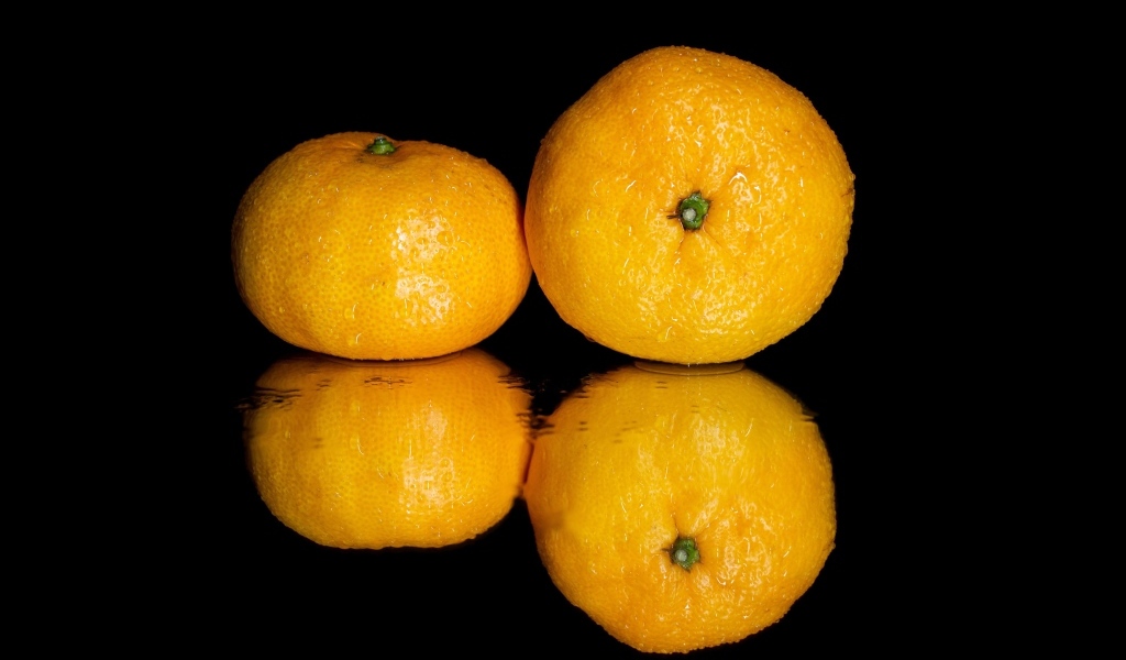 Два мандарина на черной зеркальной поверхности 