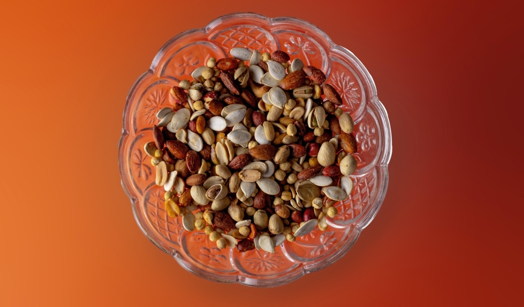 Разные орехи в стеклянной посуде на оранжевом фоне