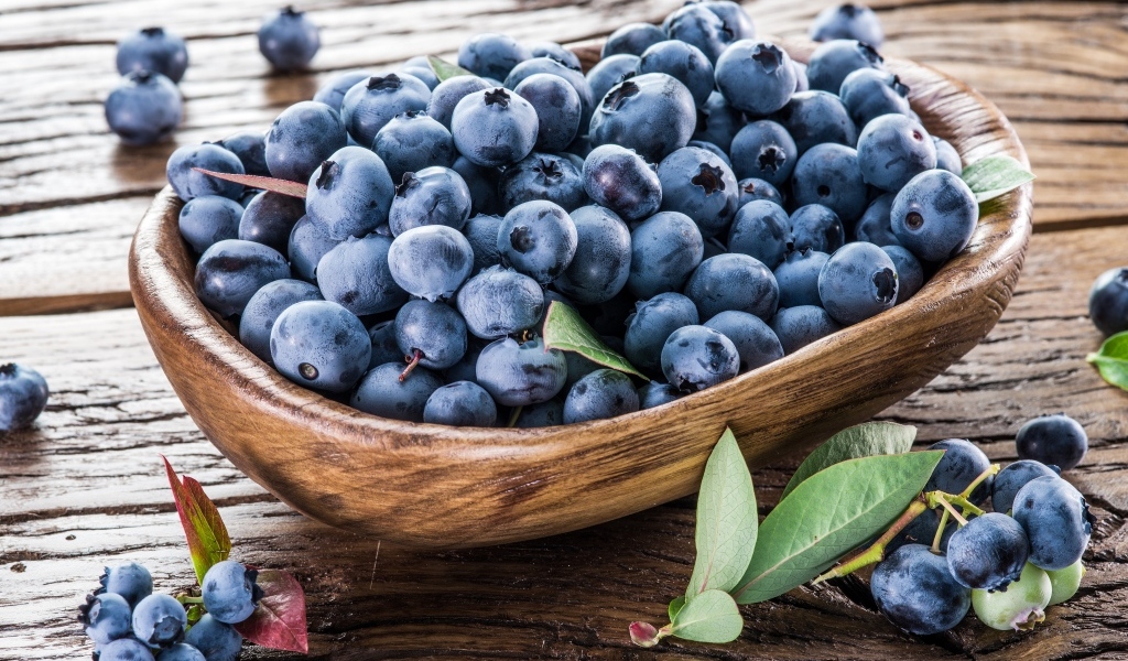 Деревянная тарелка с ягодами черники на столе