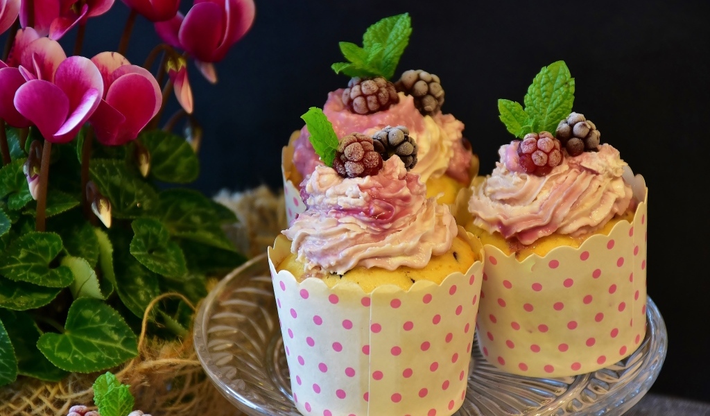 Маффины с кремом и ягодами малины на столе с цветами