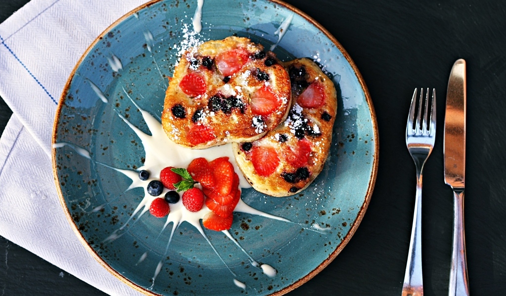 Оладьи на тарелке с ягодами и сметаной