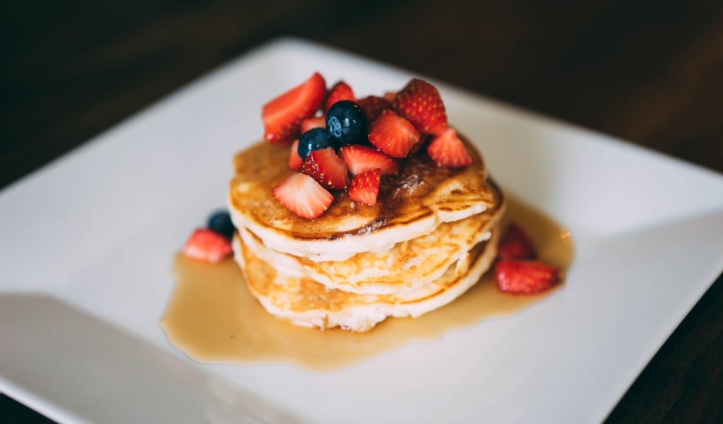 Оладьи с кусочками клубники, медом и черникой на тарелке