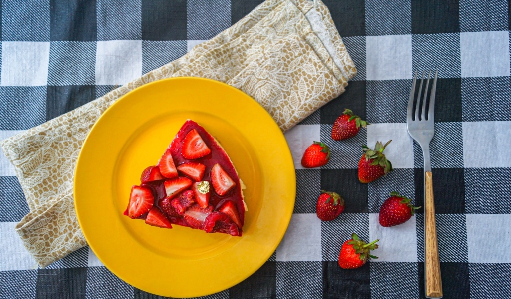 Кусок чизкейка с клубникой на желтой тарелке 