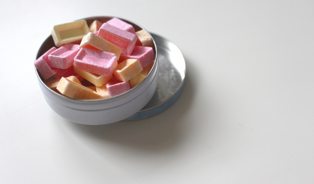 Розовые и оранжевые конфеты в коробке на сером фоне