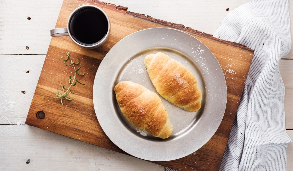 Два круассана на тарелке с чашкой кофе