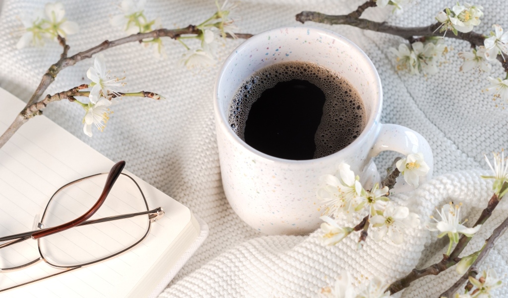 Чашка кофе с цветущей веткой на столе