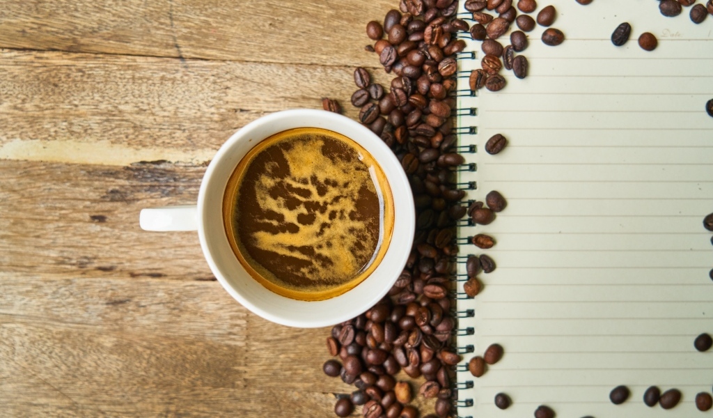 Чашка кофе на столе с зернами и блокнотом