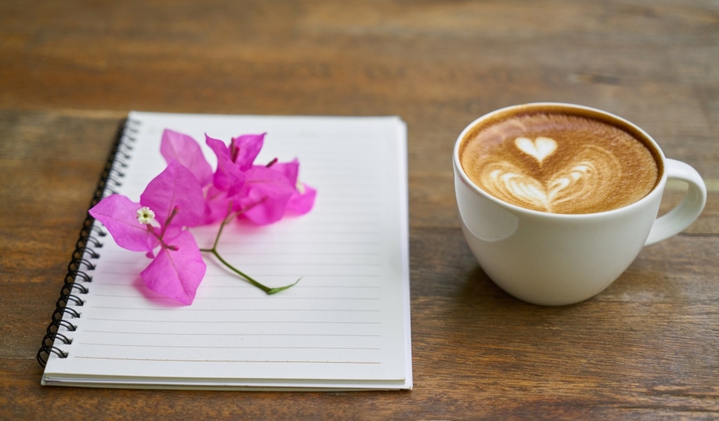 Чашка кофе на столе с блокнотом и цветами