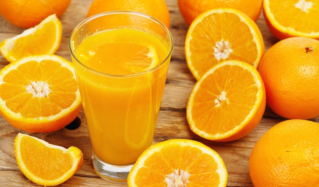 Стакан свежевыжатого сока на столе с половинками апельсина