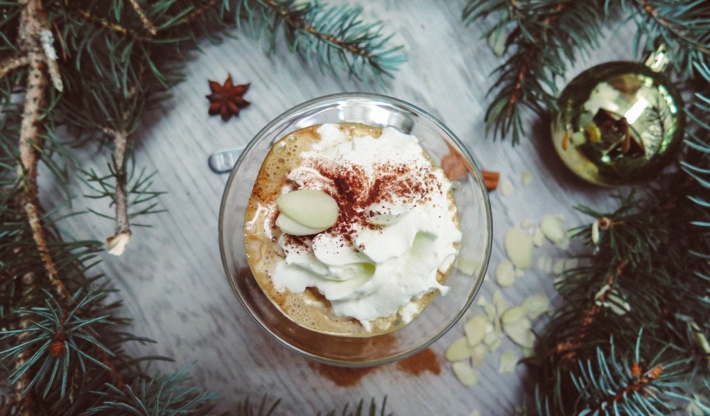 Горячий кофе с взбитыми сливками в чашке на столе с еловыми ветками