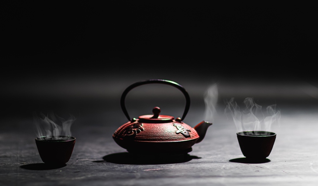 Чайник с горячим чаем на черном фоне