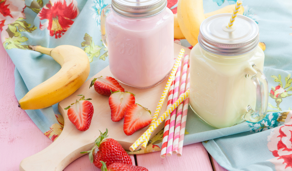 Две банки смузи на столе с бананом и ягодами клубники