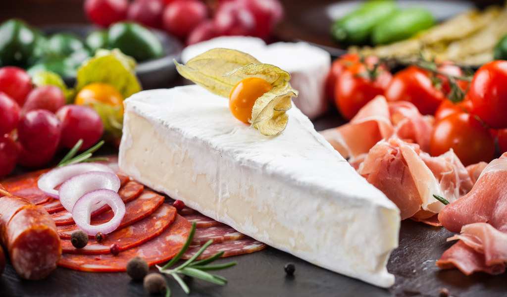 Кусок сыра на столе с овощами и колбасой