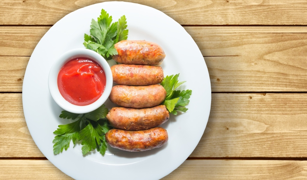 Сардельки на тарелке с соусом и петрушкой