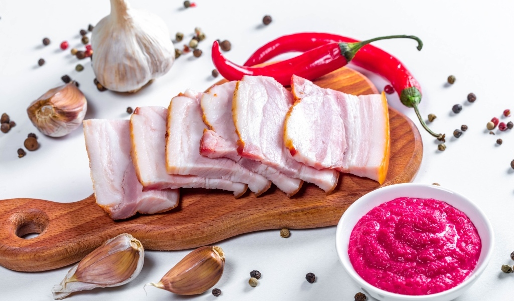 Нарезанное сало на столе с чесноком, хреном и красным перцем