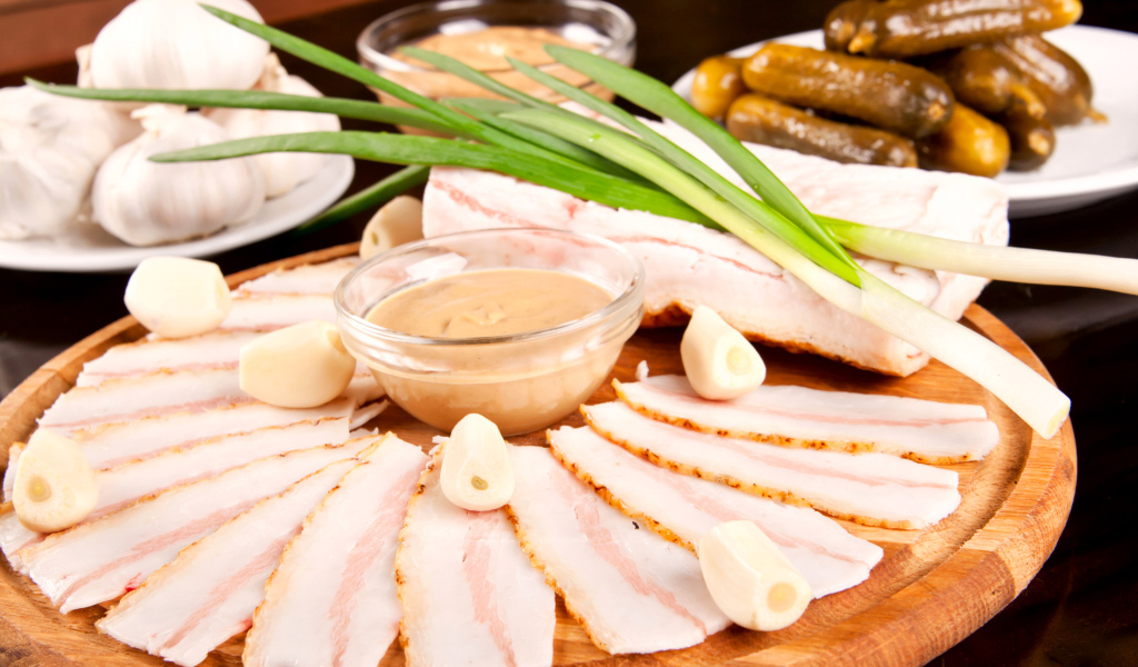 Нарезанное сало с чесноком и солеными огурцами на столе