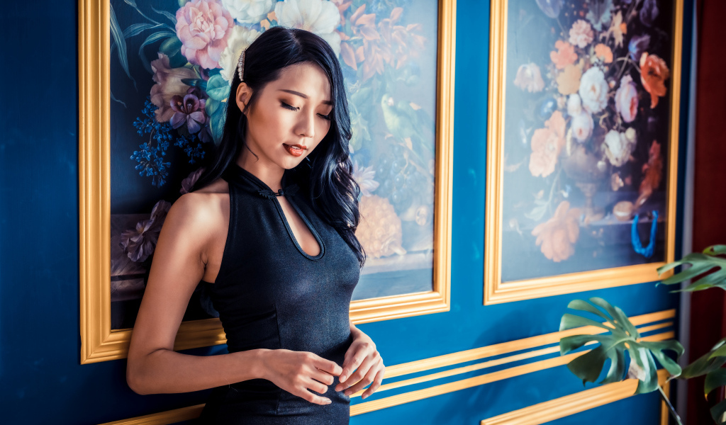 Красивая девушка азиатка в черном платье стоит у картины 