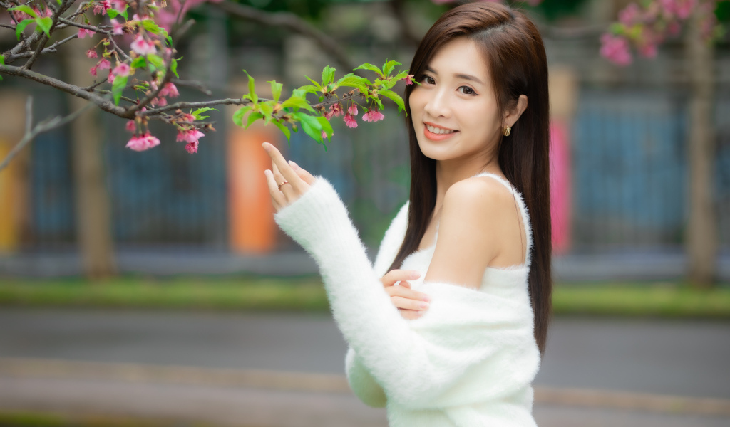 Красивая азиатка в белом свитере стоит у ветки дерева