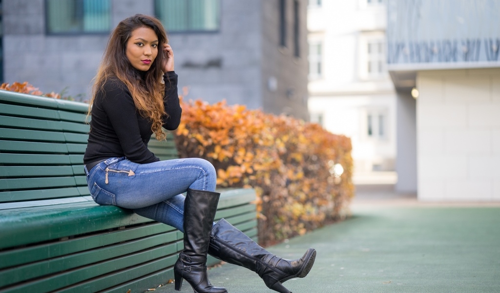 Брюнетка в синих джинсах сидит на лавке