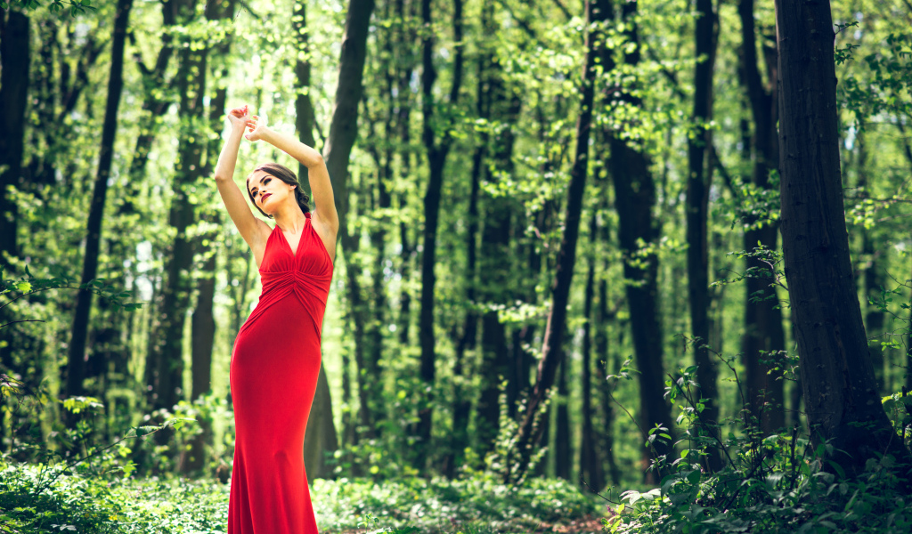 Девушка в красивом красном платье стоит в лесу