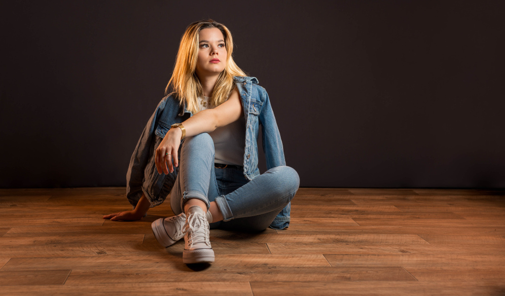 Девушка в джинсовом костюме сидит на полу