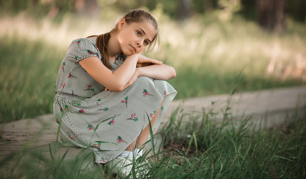 Девушка в платье сидит у зеленой травы