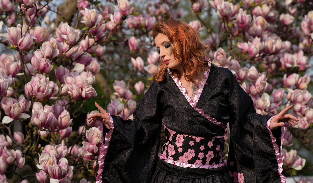 Девушка в кимоно стоит у куста с цветами магнолии