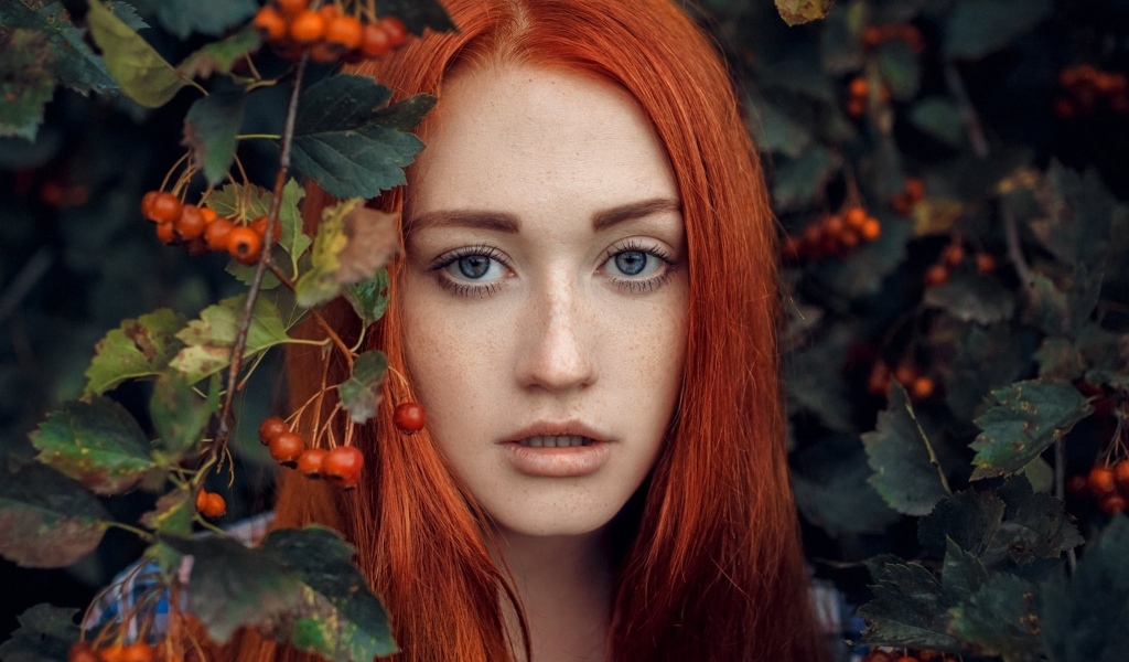 Рыжеволосая девушка стоит у куста с боярышником