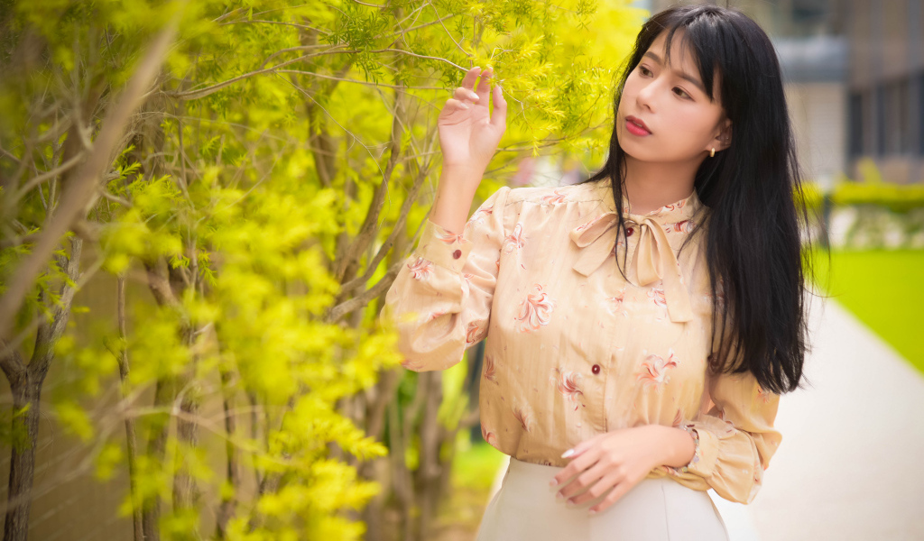 Молодая девушка азиатка стоит у дерева с зелеными листьями