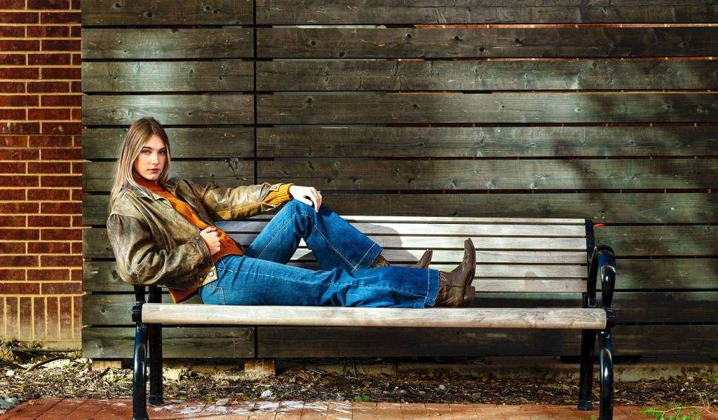 Молодая девушка в синих джинсах лежит на лавке