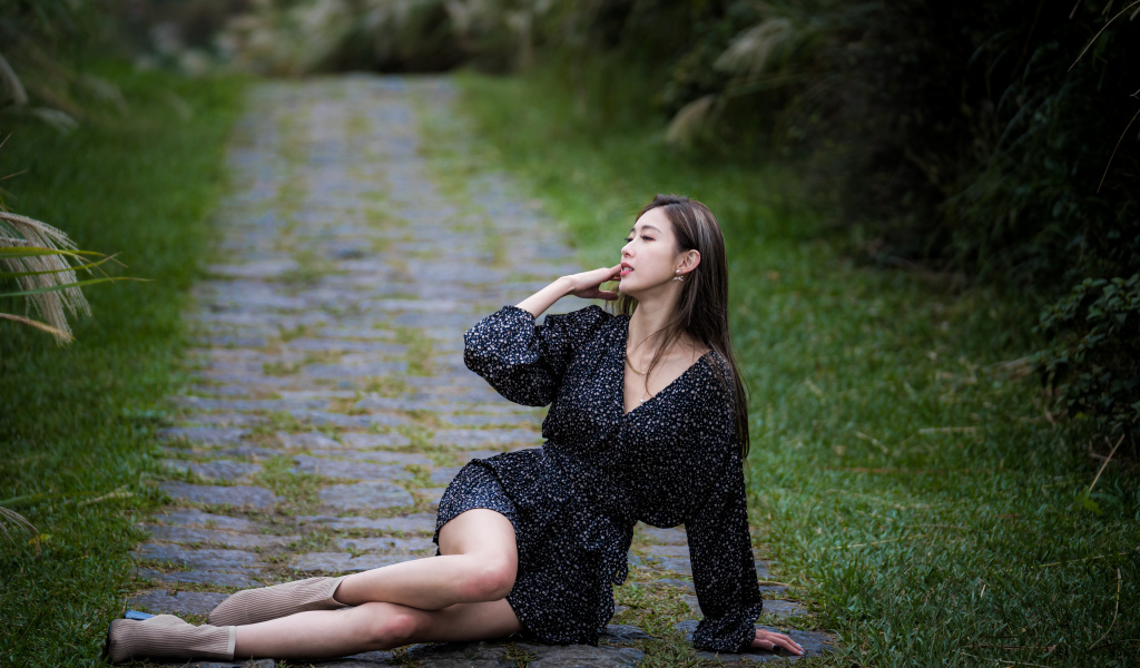 Девушка азиатка в платье лежит на дороге в парке