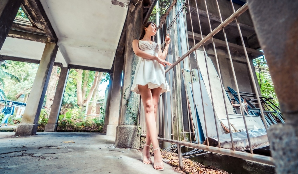 Девушка азиатка в платье стоит у решетки 