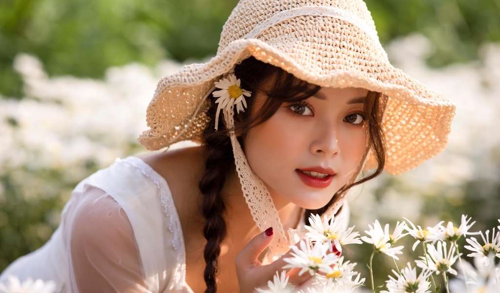 Девушка азиатка в шляпке на поле с ромашками