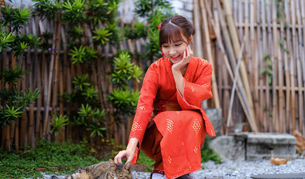 Девушка азиатка в красном платье гладит кота