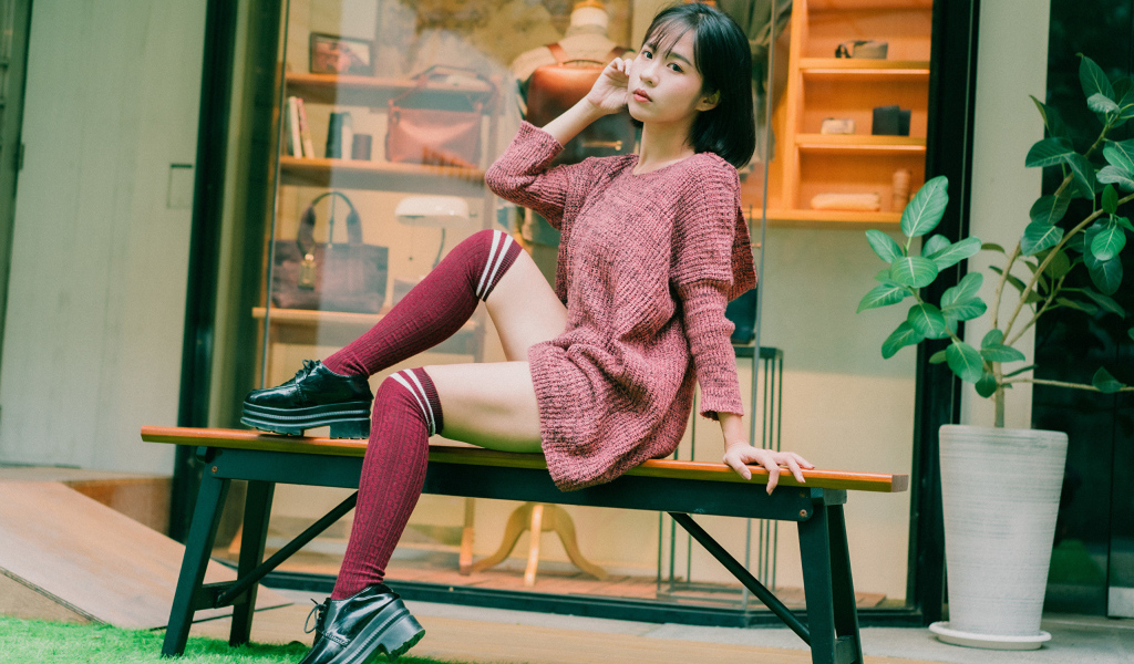 Девушка азиатка в теплом свитере сидит на лавке