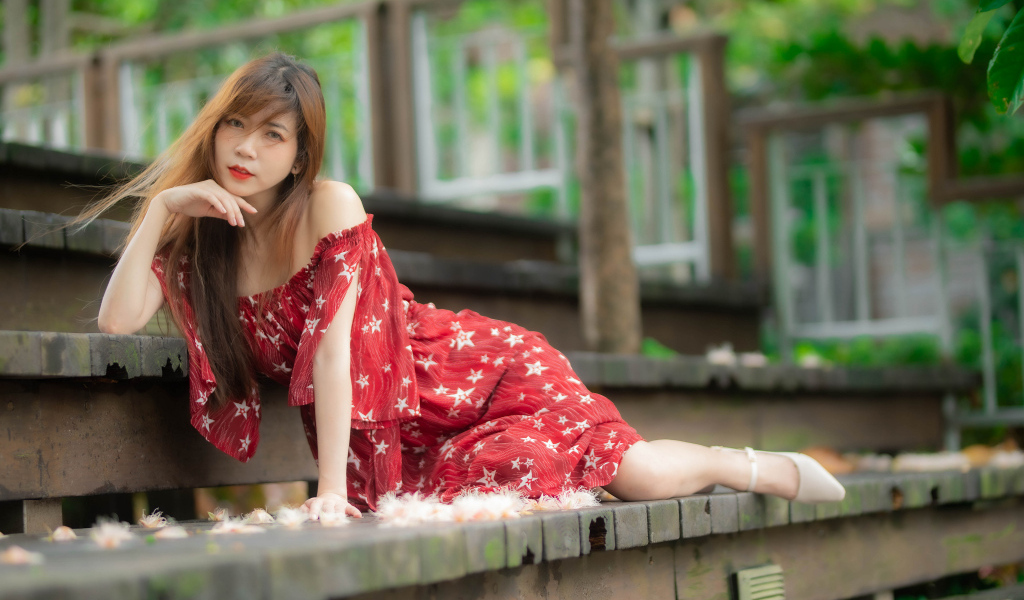 Девушка азиатка лежит на ступеньках в красном платье