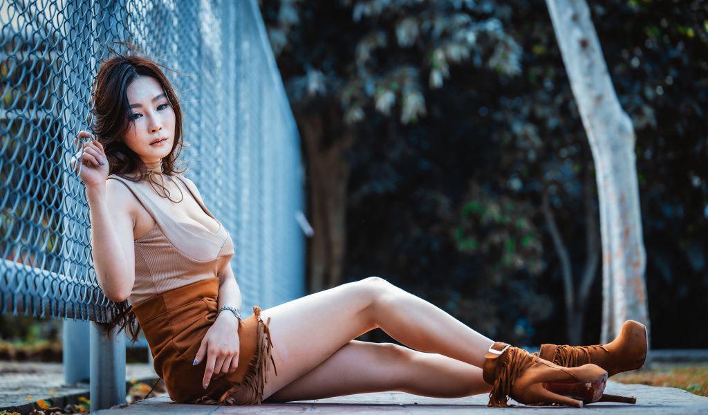 Девушка азиатка сидит на земле у сетки
