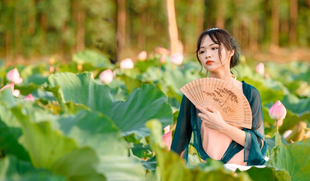 Девушка азиатка с веером в зеленых листьях лотоса