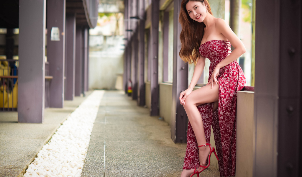 Азиатка в платье стоит у окна