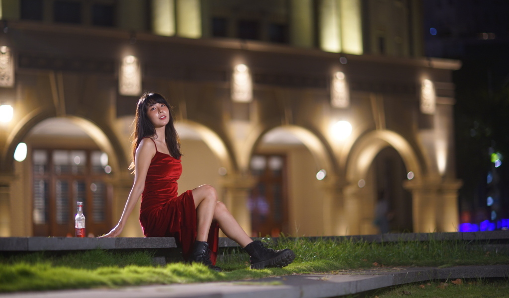 Азиатка в длинном красном платье сидит на ступенях