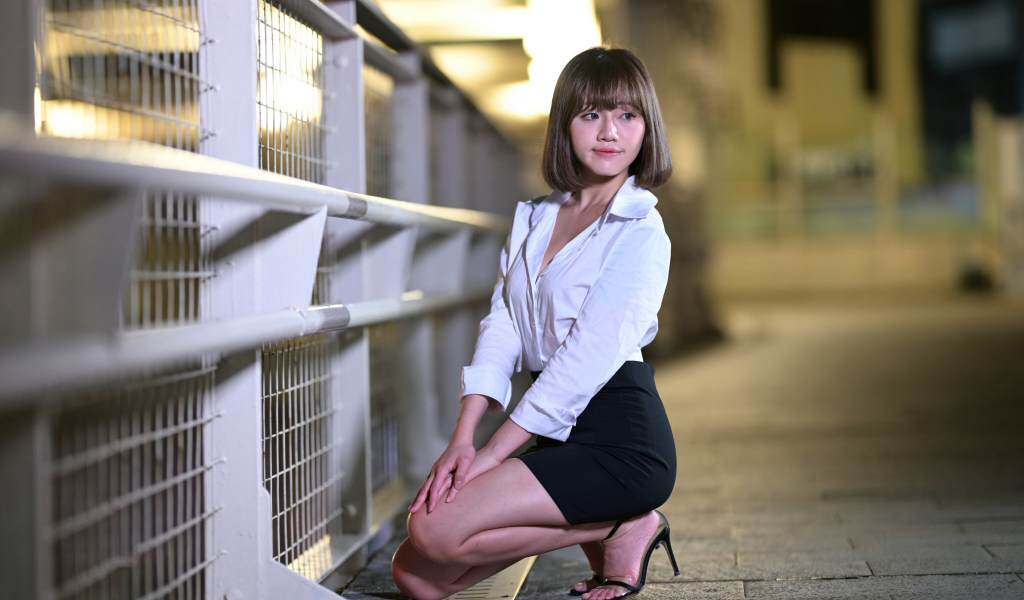 Азиатка в белой блузке и черной юбке сидит на корточках