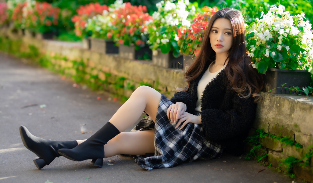 Азиатка сидит на асфальте у цветов